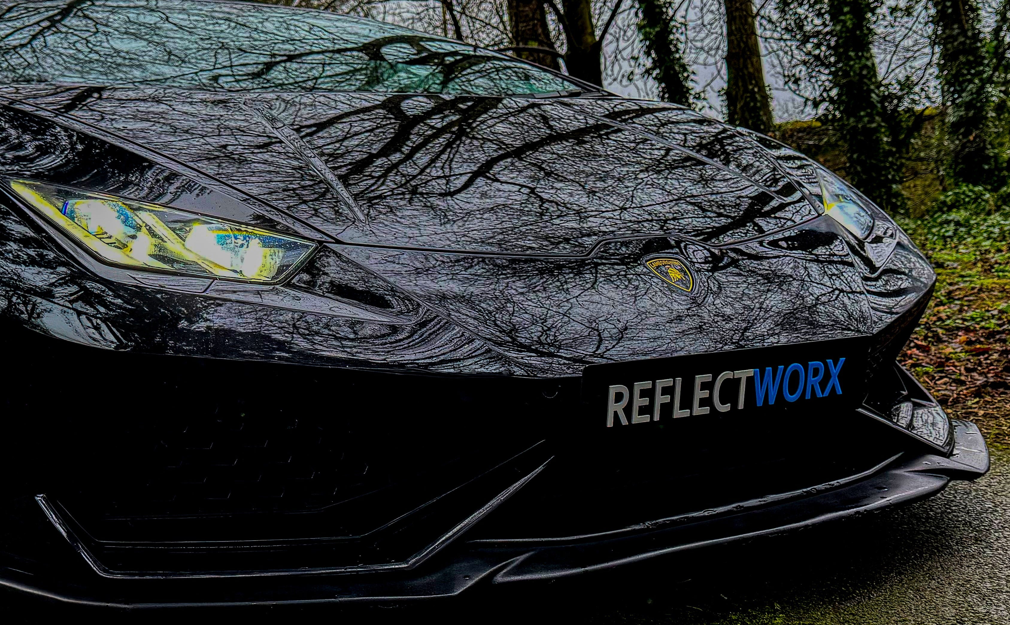 Car with 'ReflectWorx' branding on a road with trees in the background